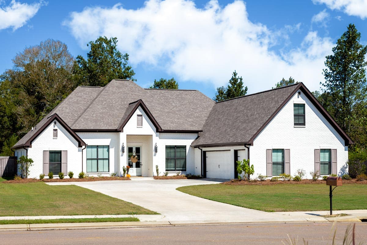 House plan exterior. Two-story, white brick home with gabled roof, dormers, and attached garage. Includes a covered front entry and shutters.