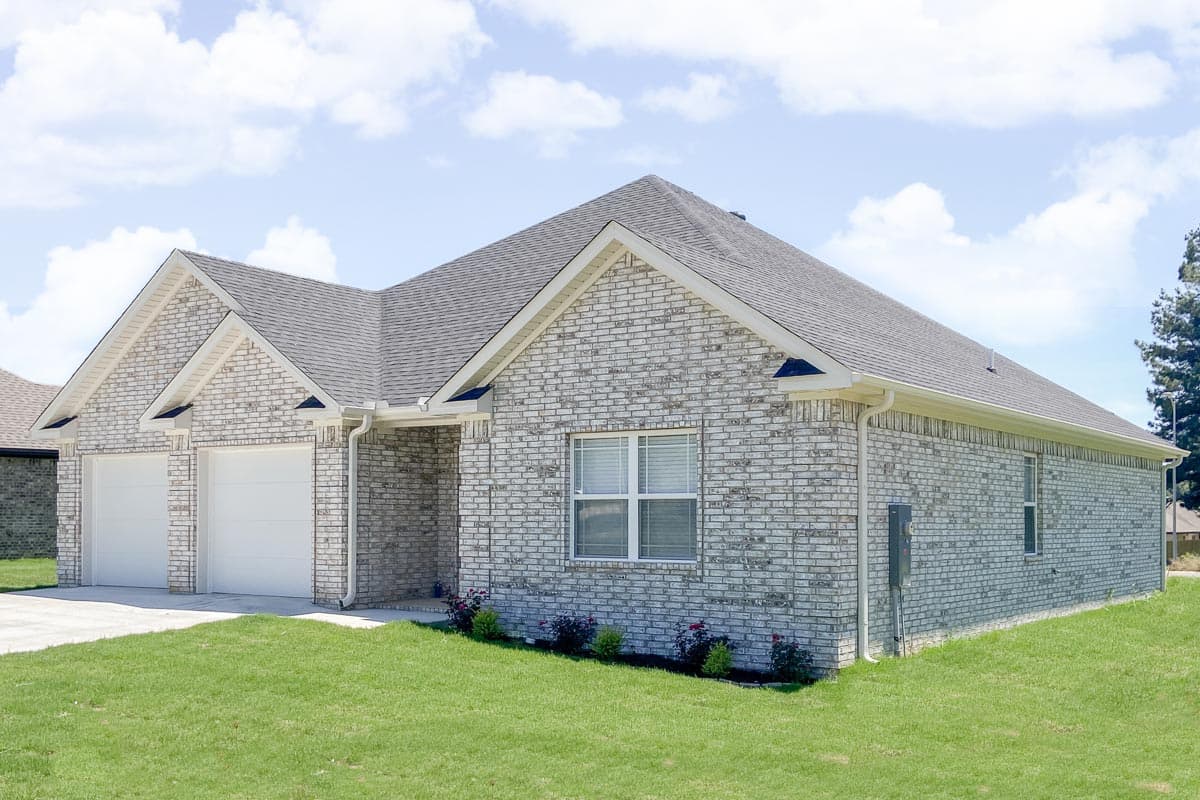 House plan exterior: Single-story home with white brick facade, three-car garage, and multiple gables.