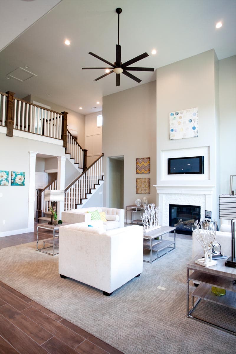 Living room with fireplace, mounted TV, two-story staircase with wood banister, and a large ceiling fan.