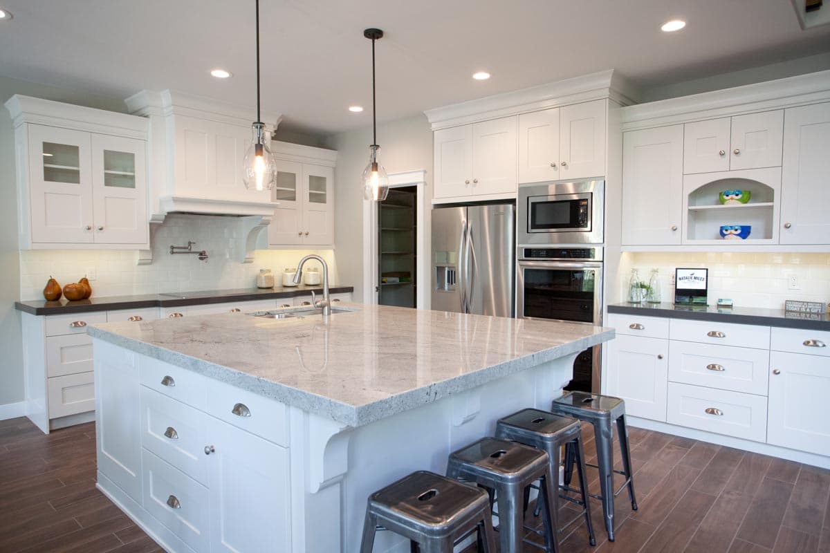 Kitchen with large island, granite countertops, white cabinetry, stainless steel appliances, and pendant lights.