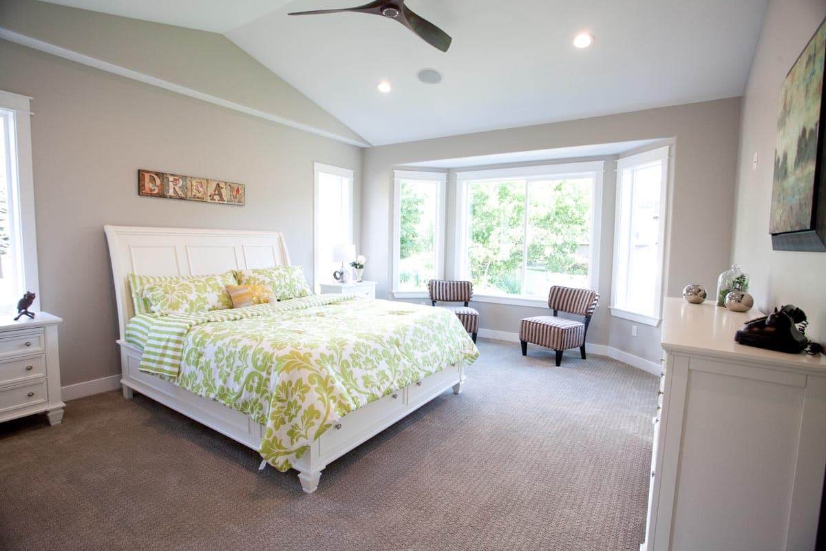 Interior view of primary bedroom with vaulted ceiling, king bed, bay window, and neutral carpet.