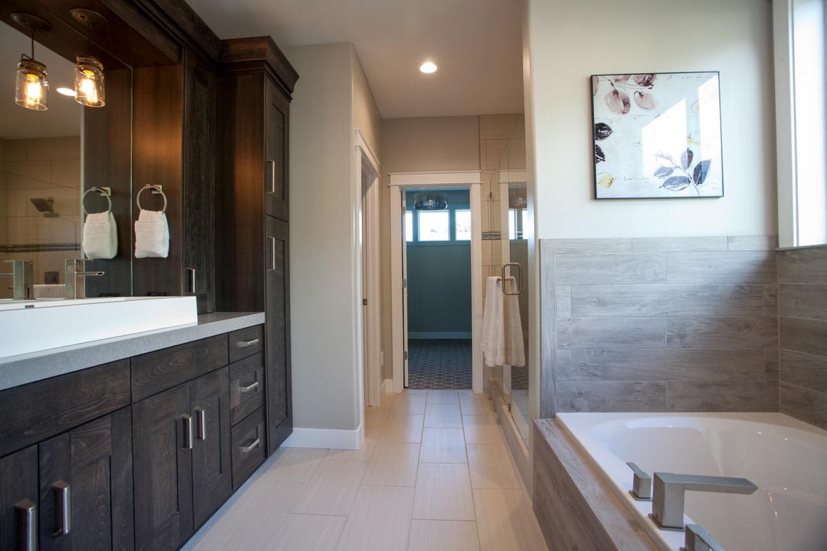 Modern bathroom with dark wood vanity, large soaking tub, glass-enclosed shower, and tiled flooring. White undermount sink.