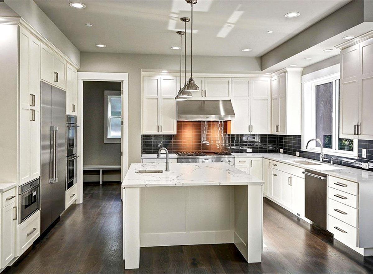Interior view of a modern kitchen with white cabinetry, a marble island, stainless steel appliances, and a tiled backsplash.