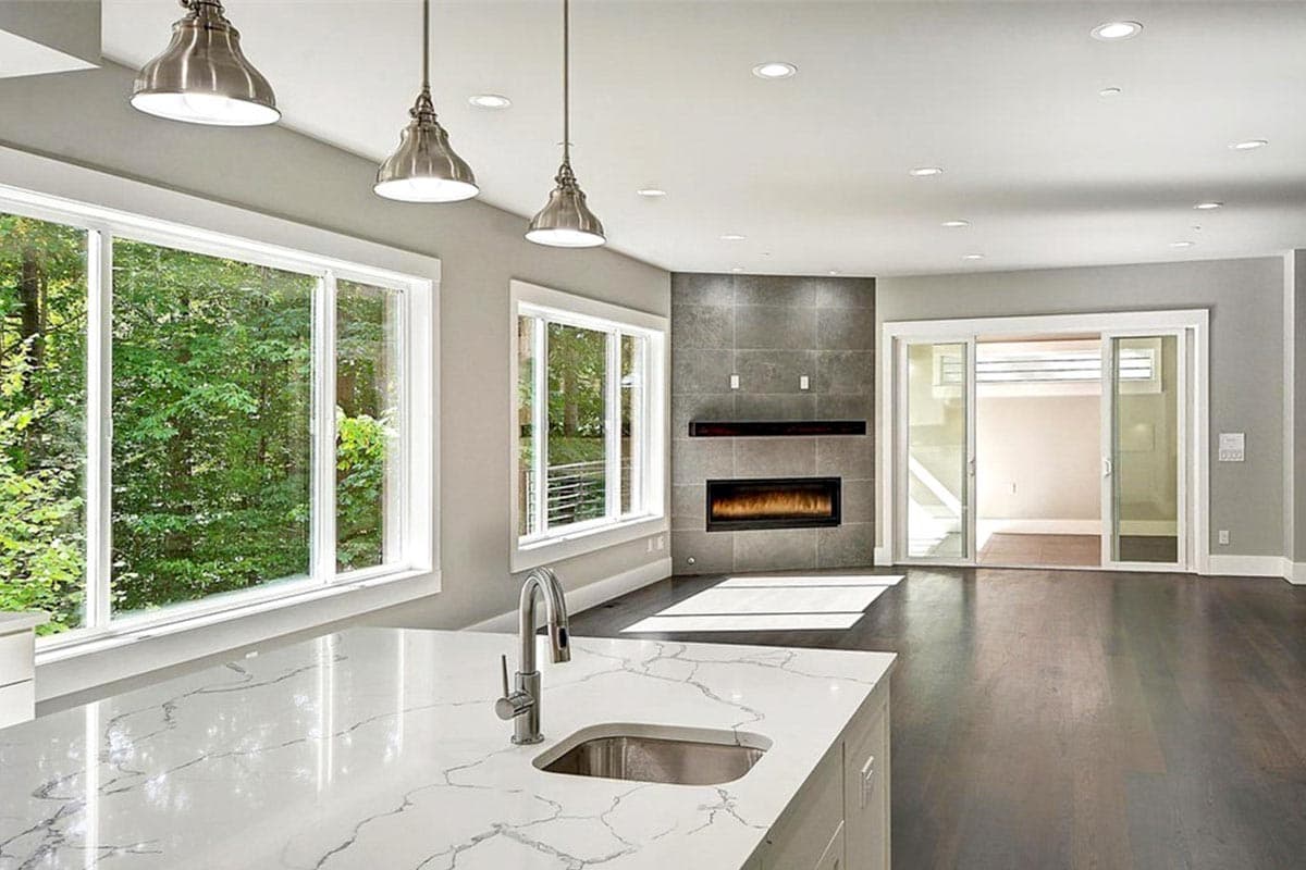 Interior rendering of an open concept living area with a modern fireplace, large windows, and a kitchen island with sink.