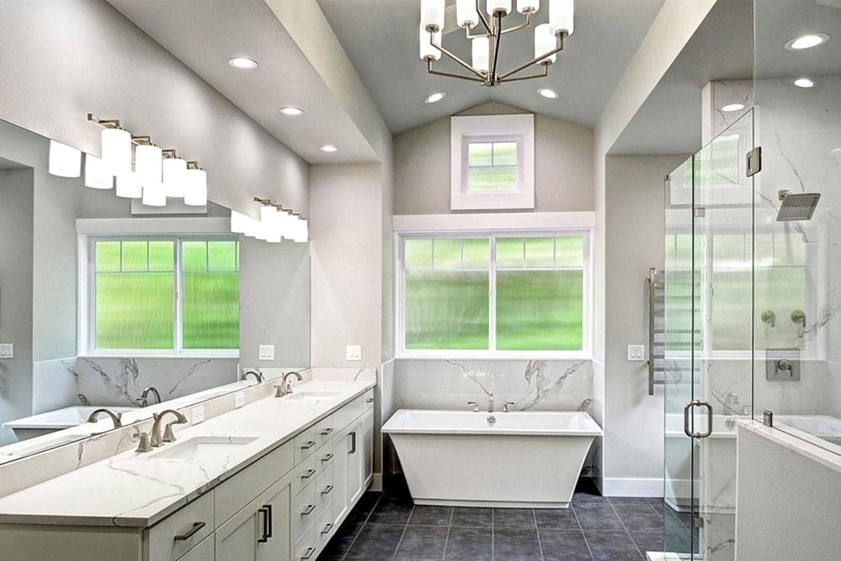 Modern bathroom featuring double vanity, freestanding tub, glass-enclosed shower with rainfall showerhead, and vaulted ceiling.
