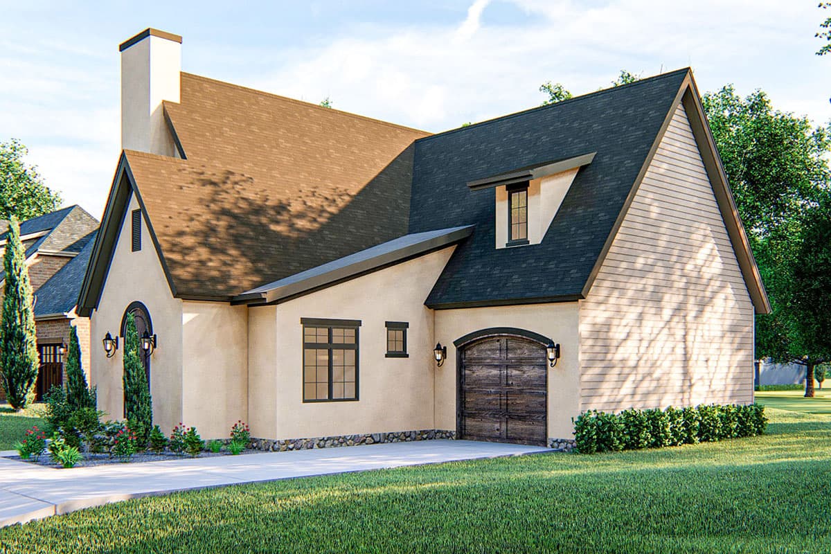 House plan exterior: stucco finish, gambrel roof, dormer window, arched garage door, and prominent chimney.