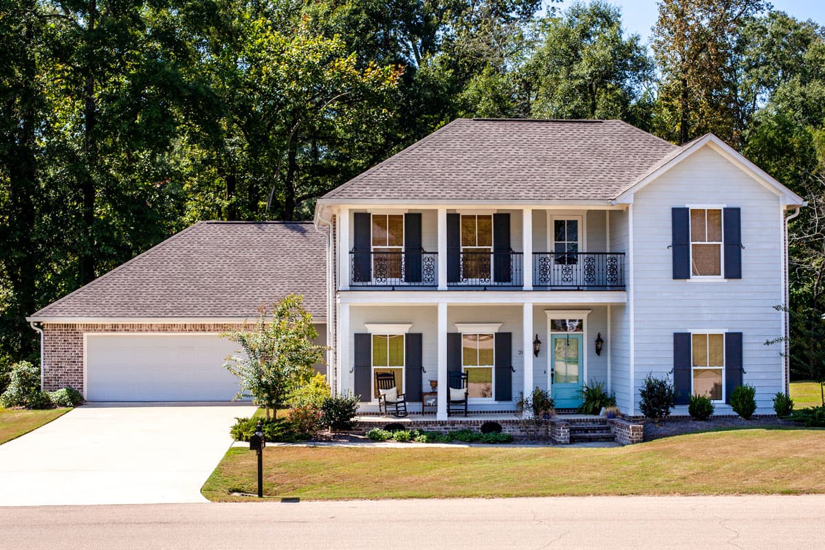 House plan exterior featuring a two-story design with a porch, gables, and a detached garage. It has a hip roof and shutters.