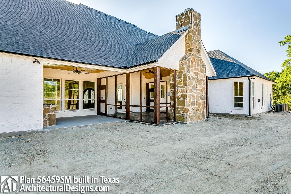 House plan exterior with white brick, prominent stone chimney, screened porch, and gabled rooflines.