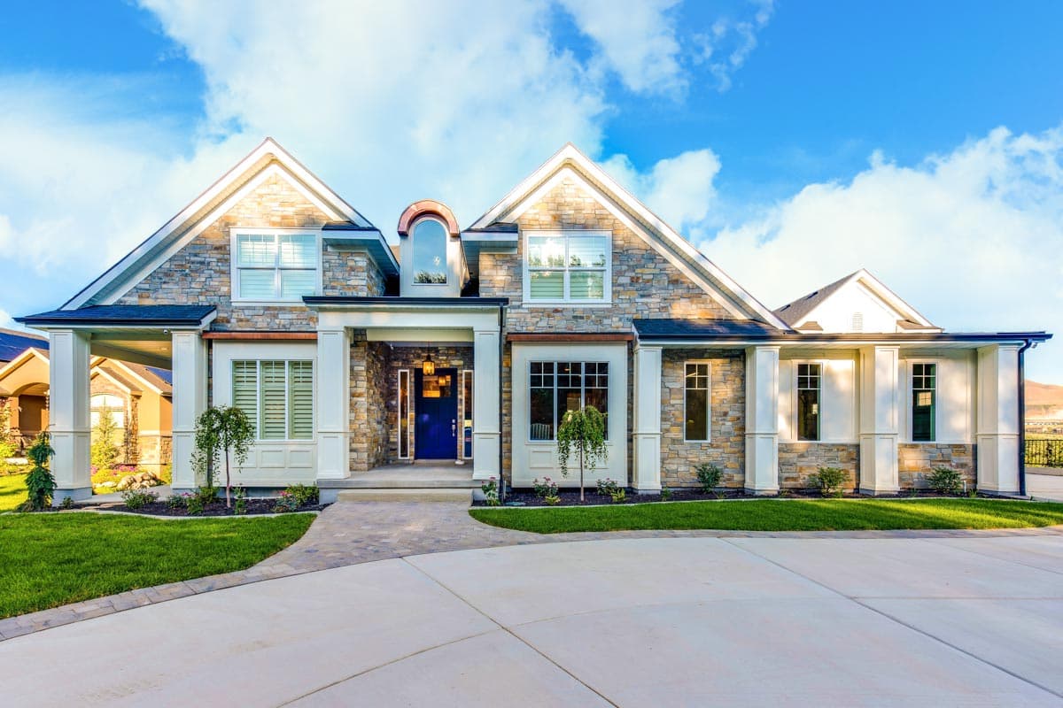 House plan exterior with stone veneer, multiple gables, arched dormer, and covered entryway with large columns.
