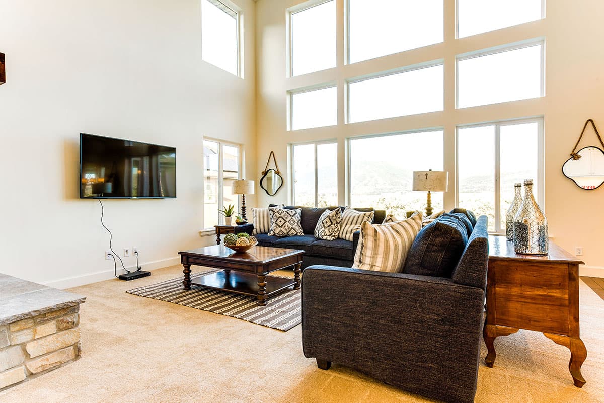 Interior living room with vaulted ceiling, floor-to-ceiling windows, sectional sofa, coffee table, and television.