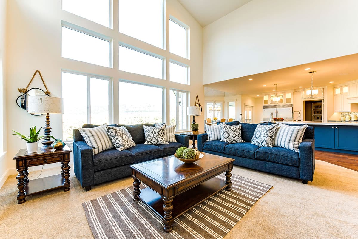 Great room with vaulted ceiling, two sofas, coffee table, and wall of windows opening to kitchen.