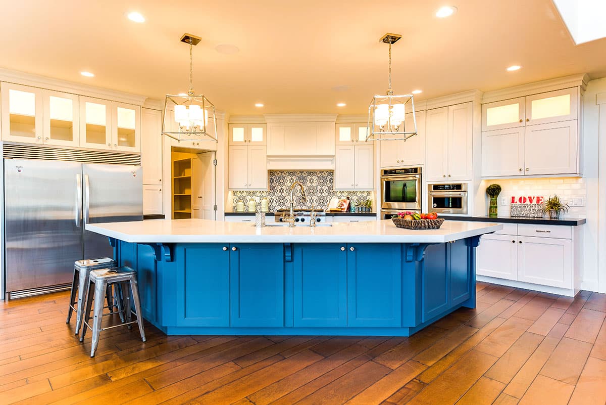 Kitchen with large blue island, stainless steel appliances, white cabinetry, and patterned tile backsplash.