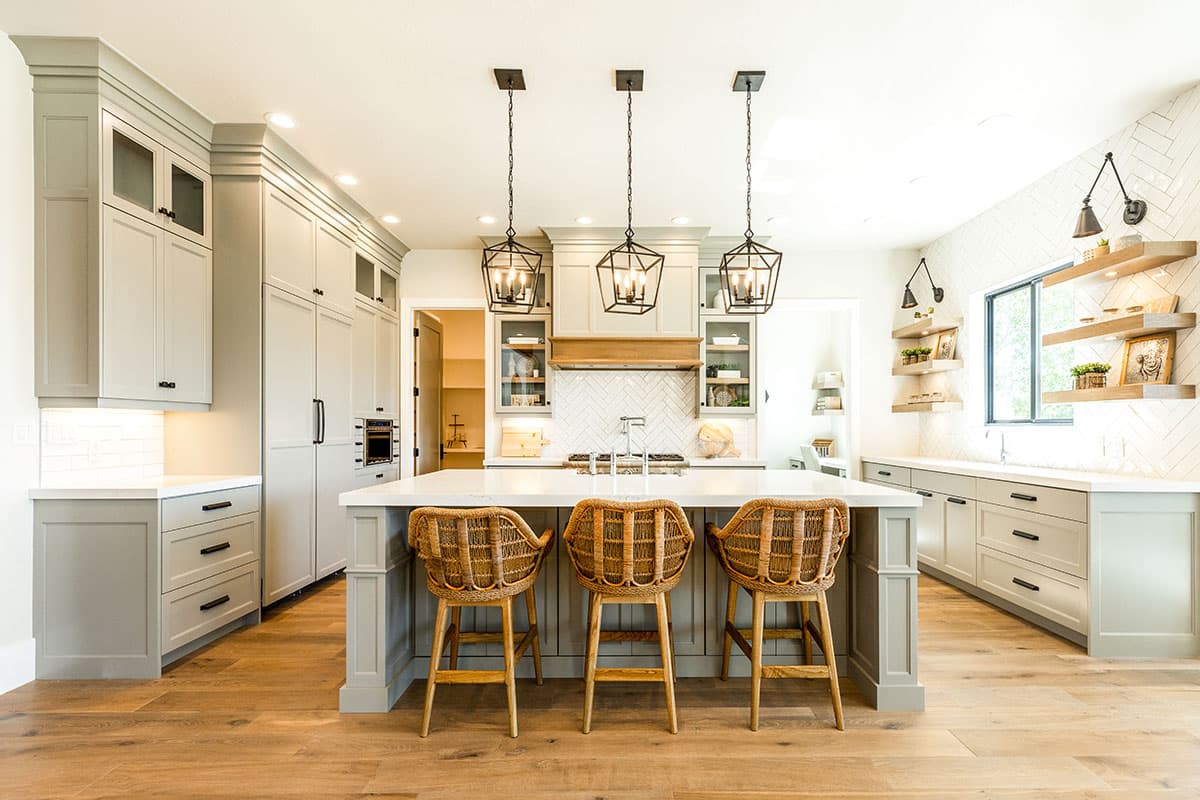 Kitchen with island, pendant lights, gray cabinetry, white countertops, herringbone tile backsplash, and open shelving.