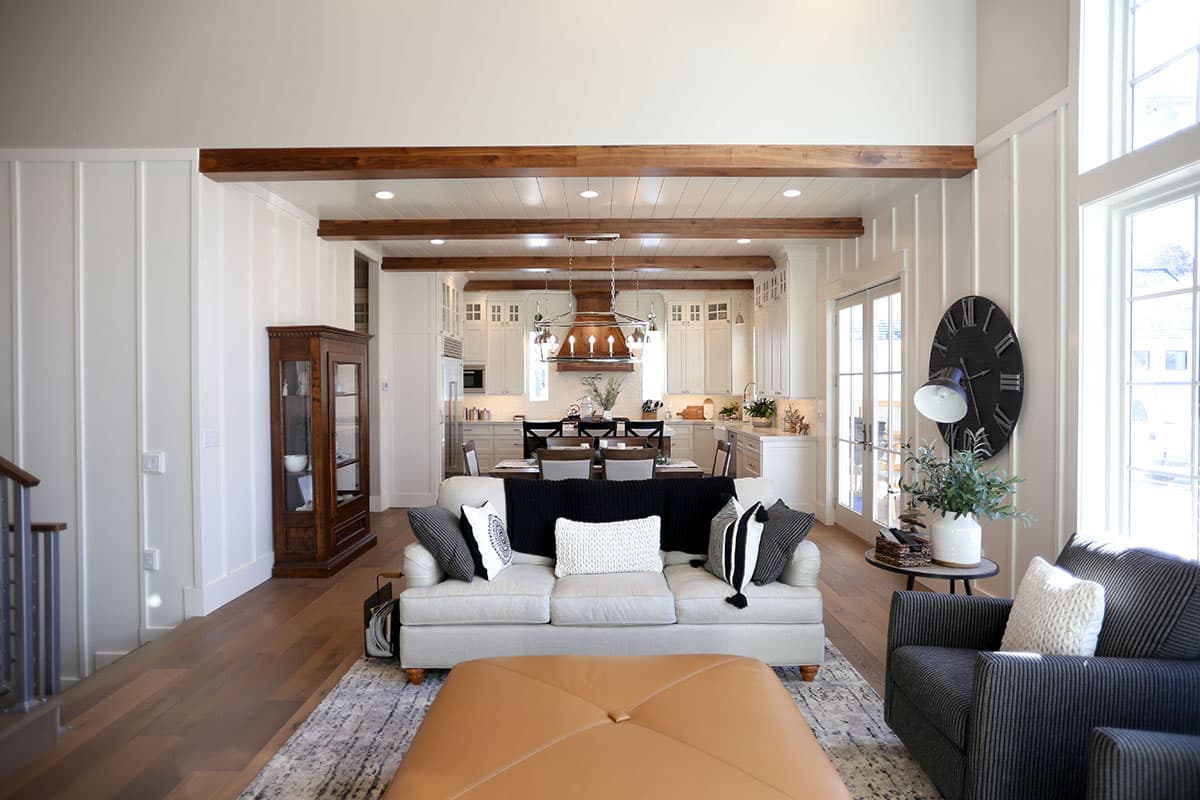 Open-concept living area with white board-and-batten walls, exposed wood beams, and a view into a modern kitchen.