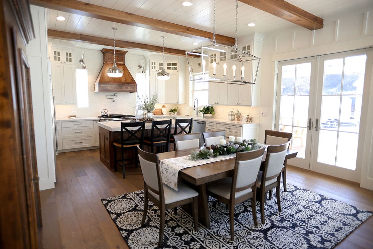 Open concept kitchen and dining area with a large island, white cabinetry, wooden ceiling beams, and French doors.