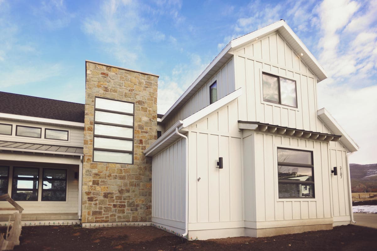 Modern Farmhouse house plan exterior with stone accent tower, vertical siding, gables, and dark-framed windows.