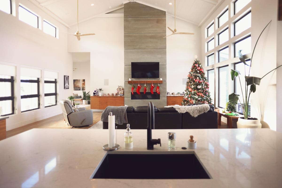 Open concept living area with vaulted ceilings, concrete fireplace, large windows, and a Christmas tree.