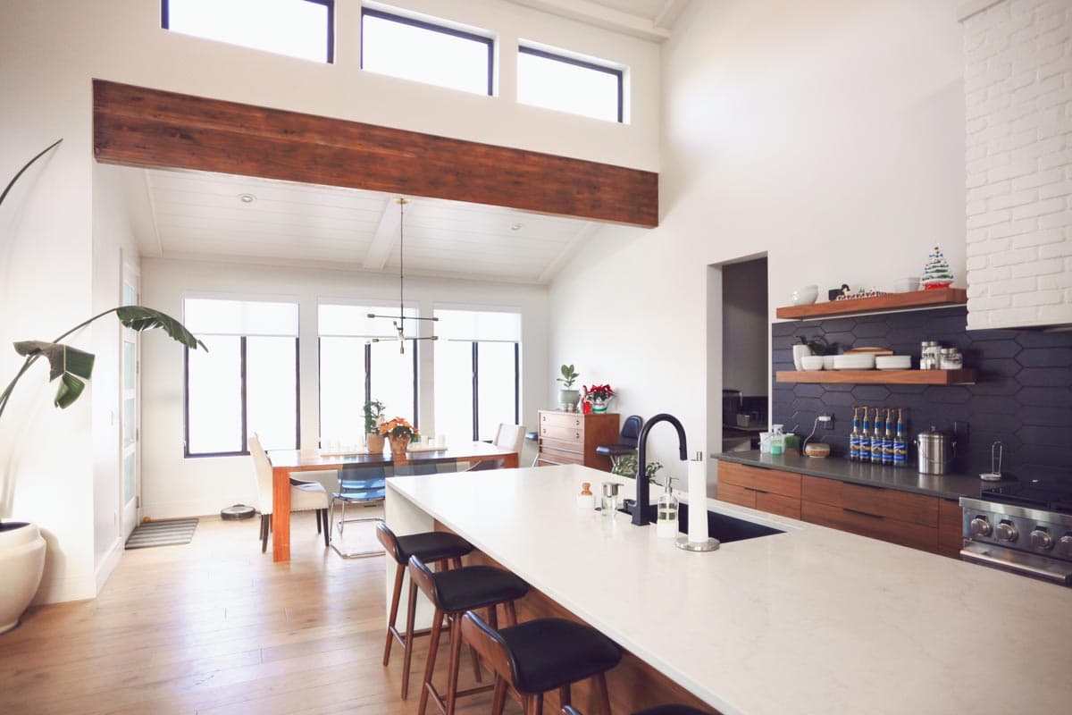 Open concept kitchen and dining area with vaulted ceilings, exposed beam, large windows, and kitchen island with seating.