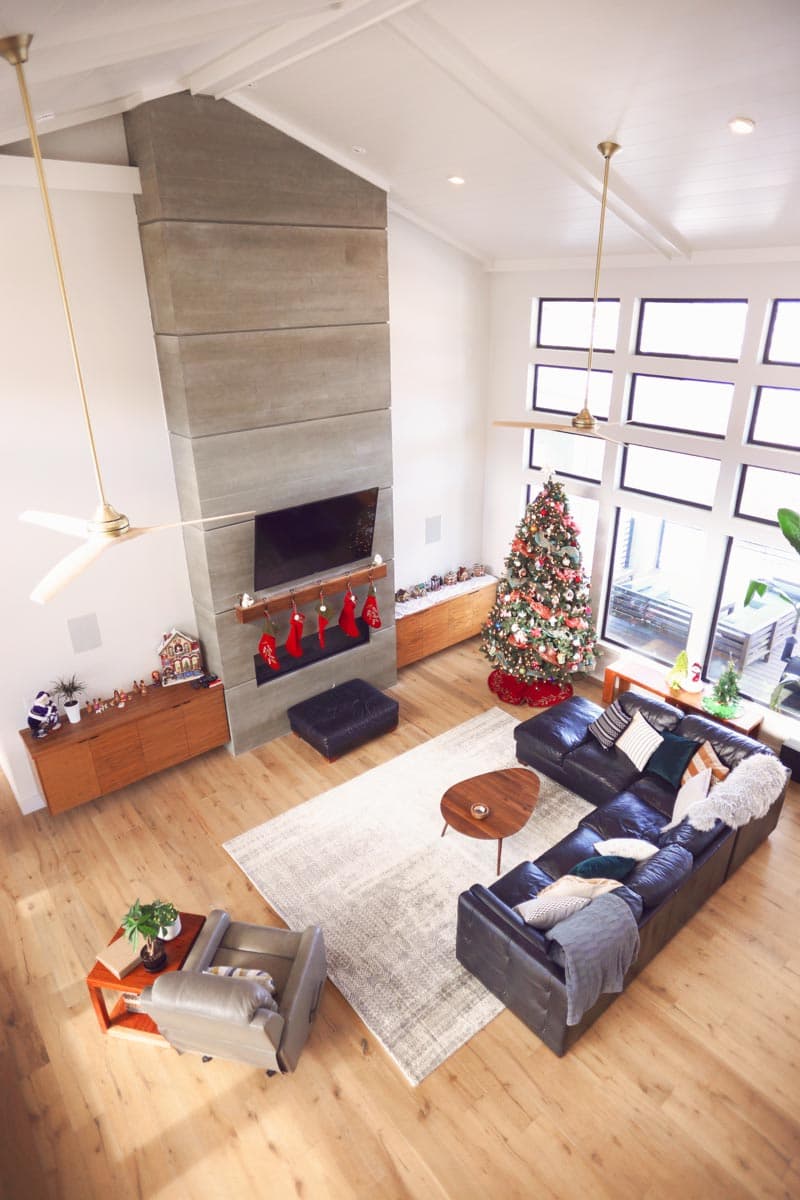 Interior view of a living room with a tall, modern fireplace, vaulted ceiling, large windows, and a Christmas tree.