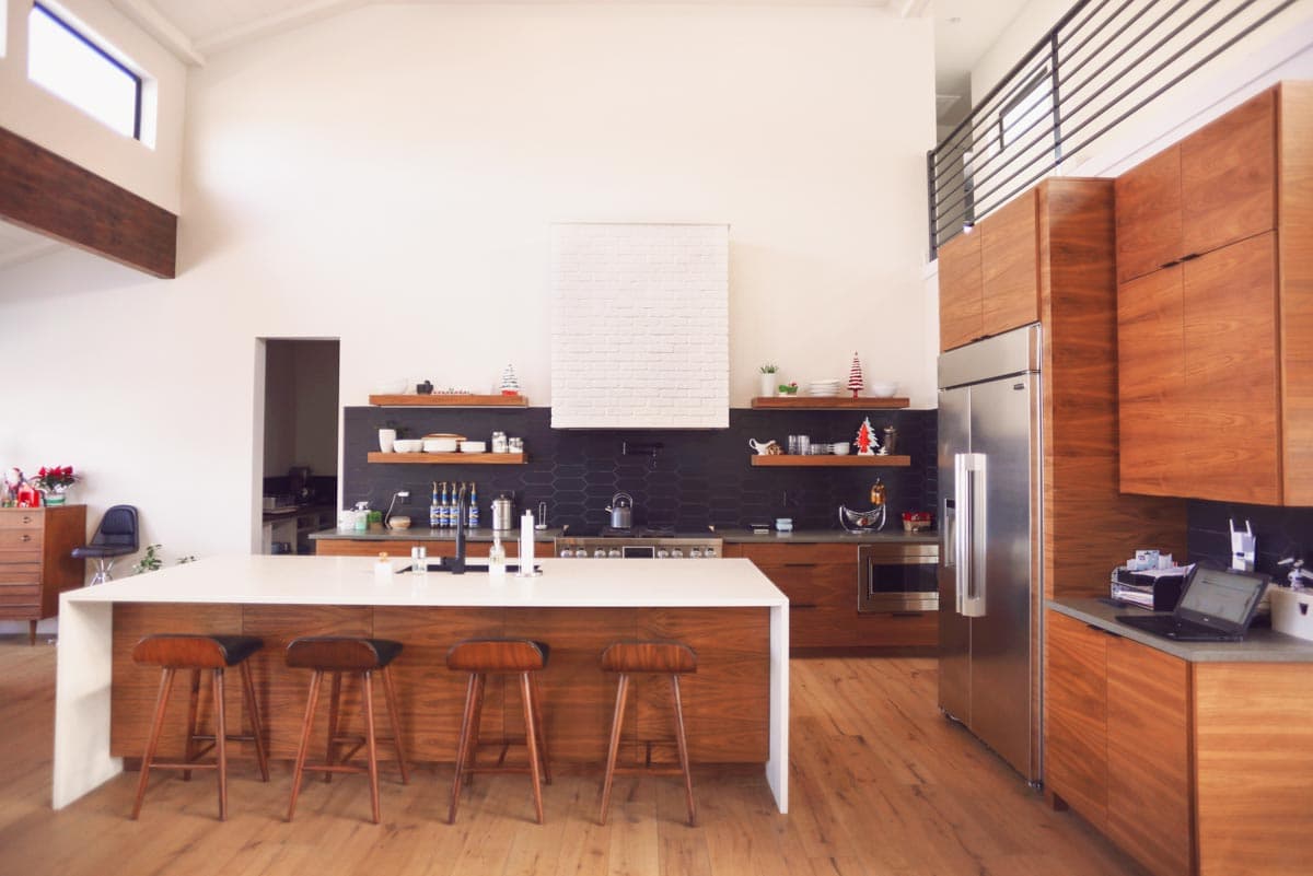 Modern kitchen with vaulted ceiling, large island with seating, wood cabinetry, stainless steel appliances, and hexagonal tile backsplash.