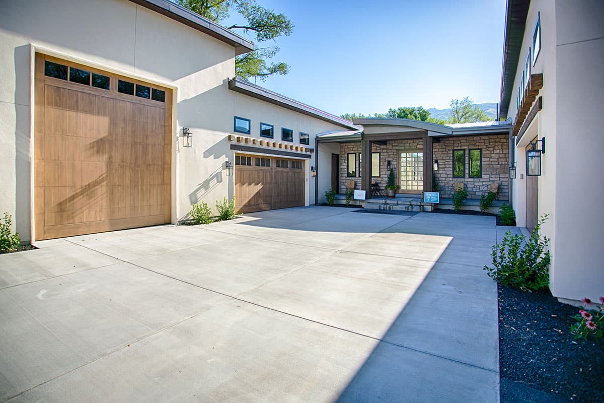 House plan exterior: Modern style with stucco, stone accents, a pitched roof, two wood garage doors, and covered entry.