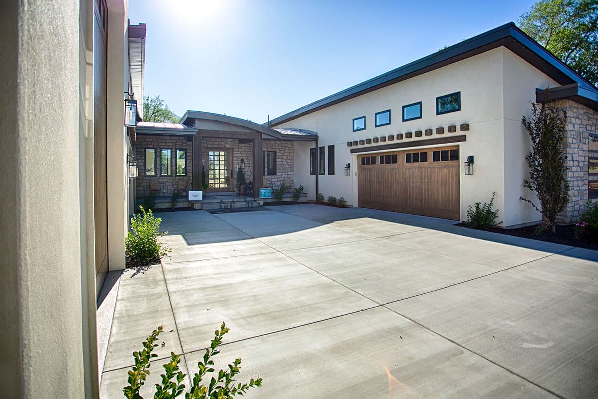 Modern house exterior with stone accents, covered entry with wood posts, and a double garage door. Features a low-pitched roof.