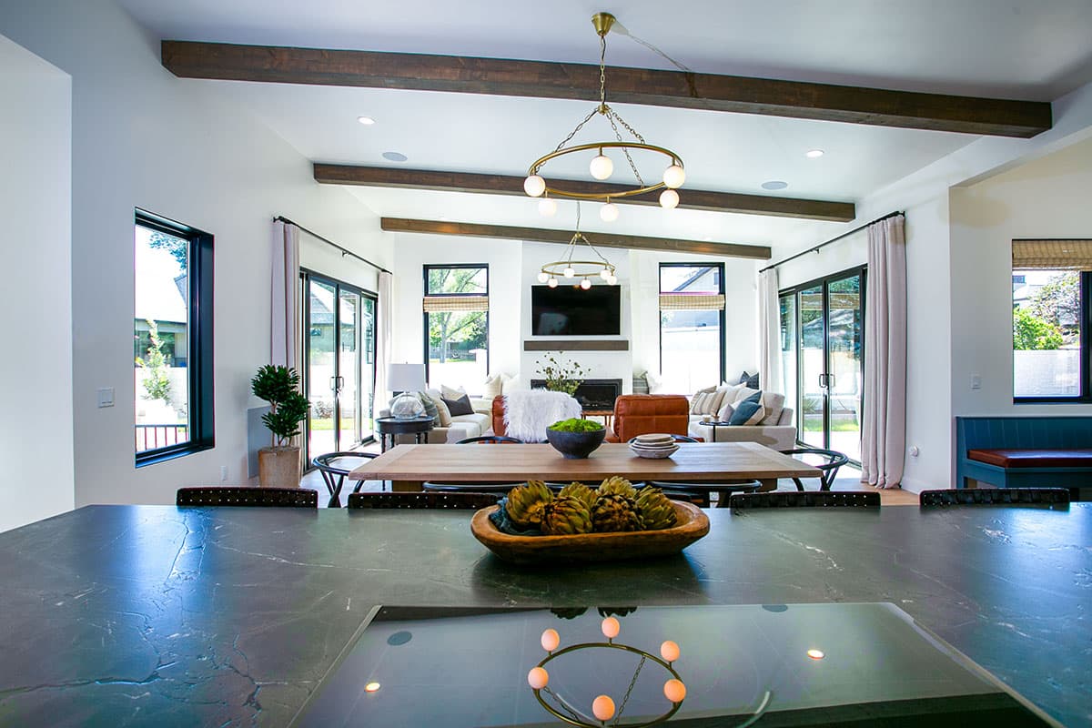 Open-concept living and dining area with a fireplace, vaulted ceiling, exposed beams, and large windows.