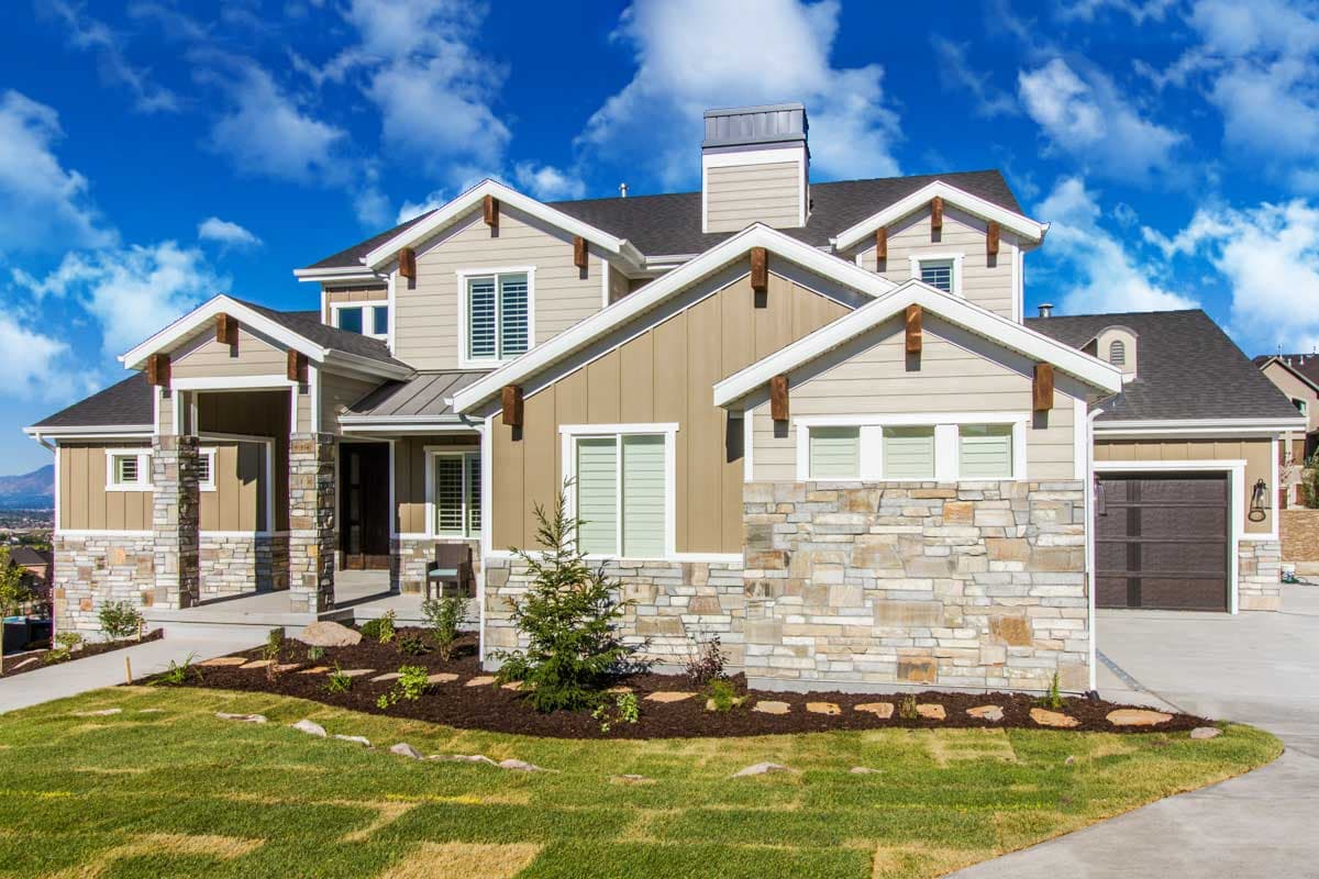 House plan exterior: Two-story home with stone and vinyl siding, prominent gables with exposed rafter tails, and a covered front entry.