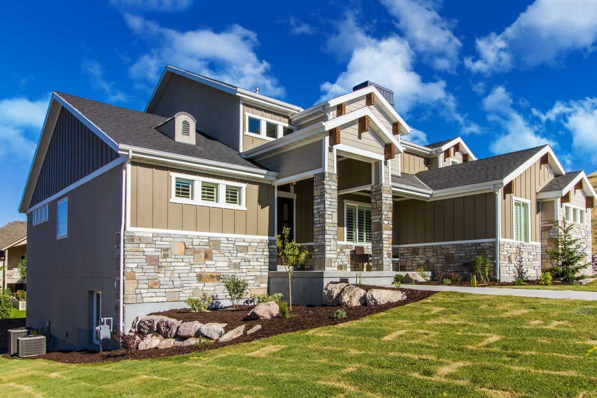 House plan exterior: Two-story home with stone and horizontal siding, prominent gabled entryway, and dormer.