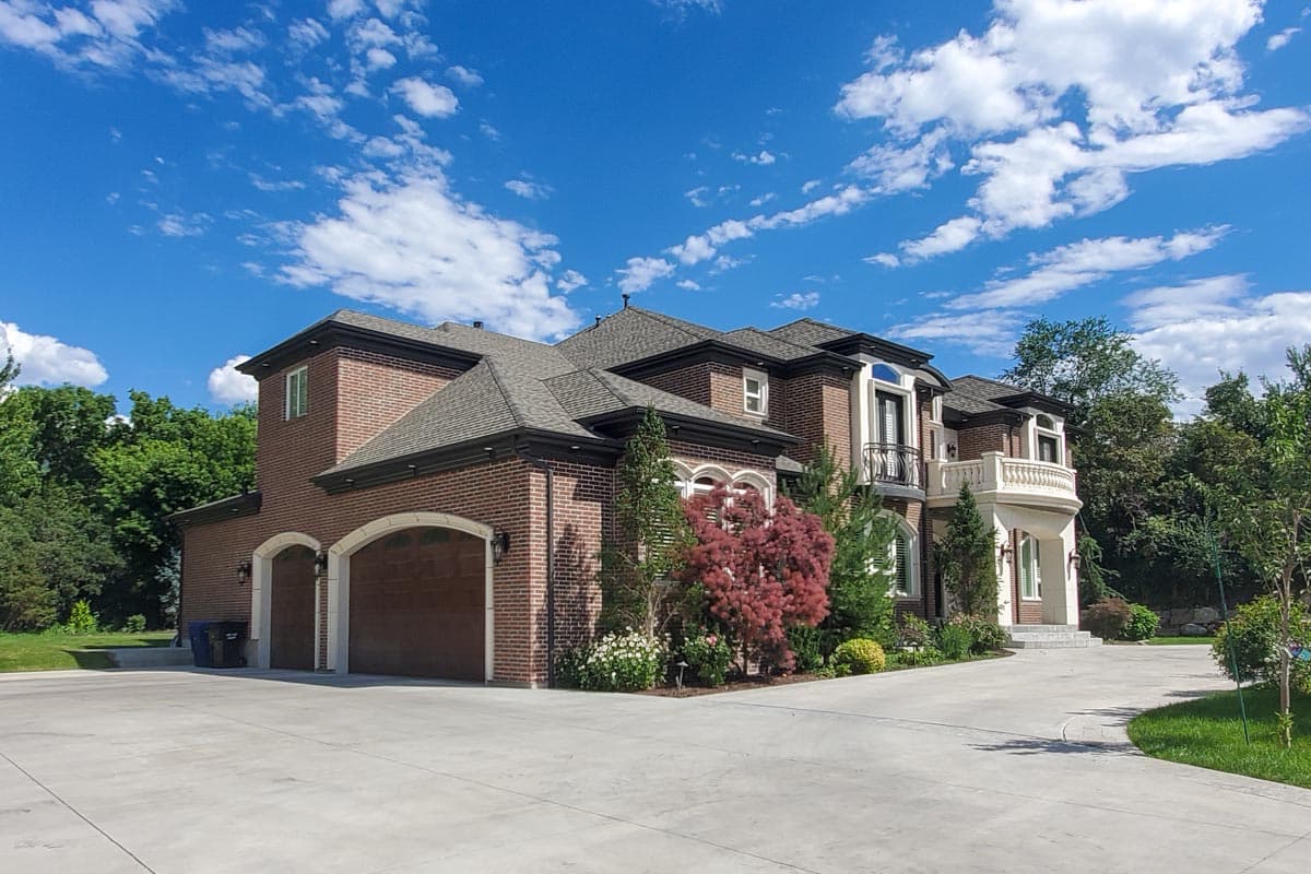 House plan exterior: Two-story brick residence with a three-car garage, arched entryways, and a Juliet balcony on the second floor.