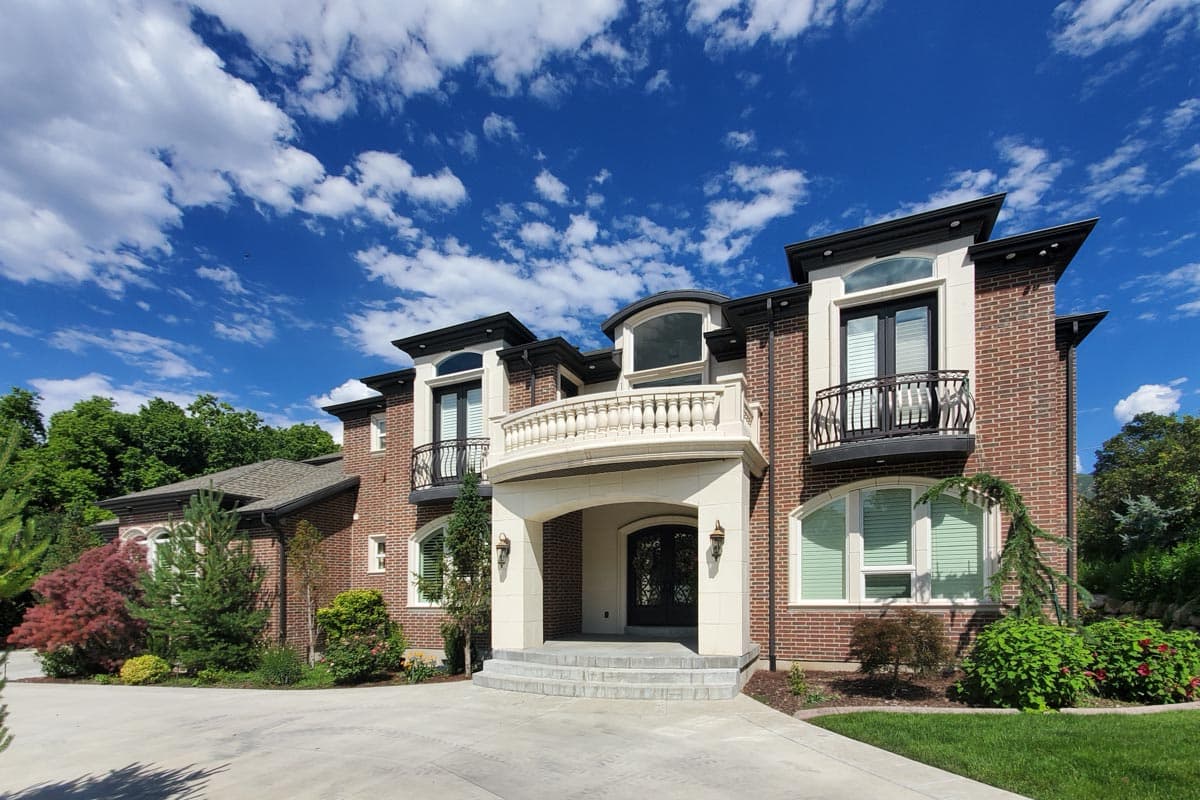 House plan exterior shows a two-story brick home with a central arched entryway, balconies, and projecting gables.