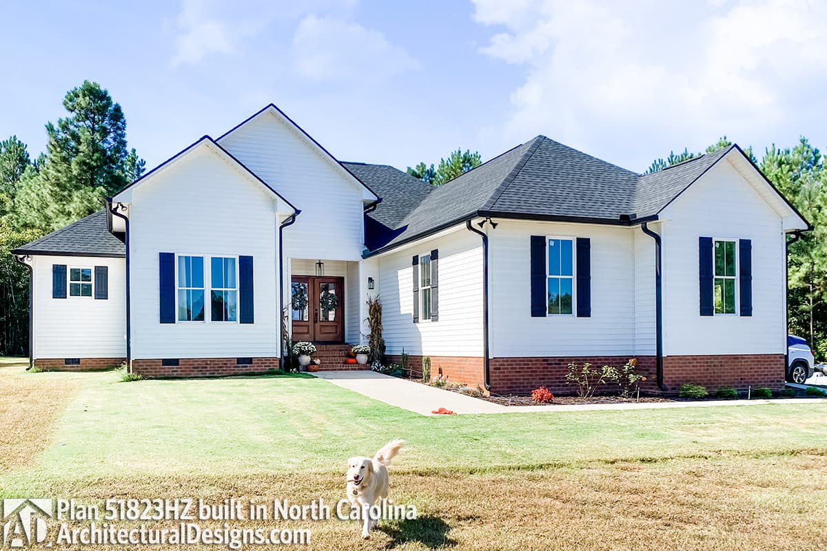 House plan exterior: White siding, gabled rooflines, central entry with double doors, and a side-facing garage.