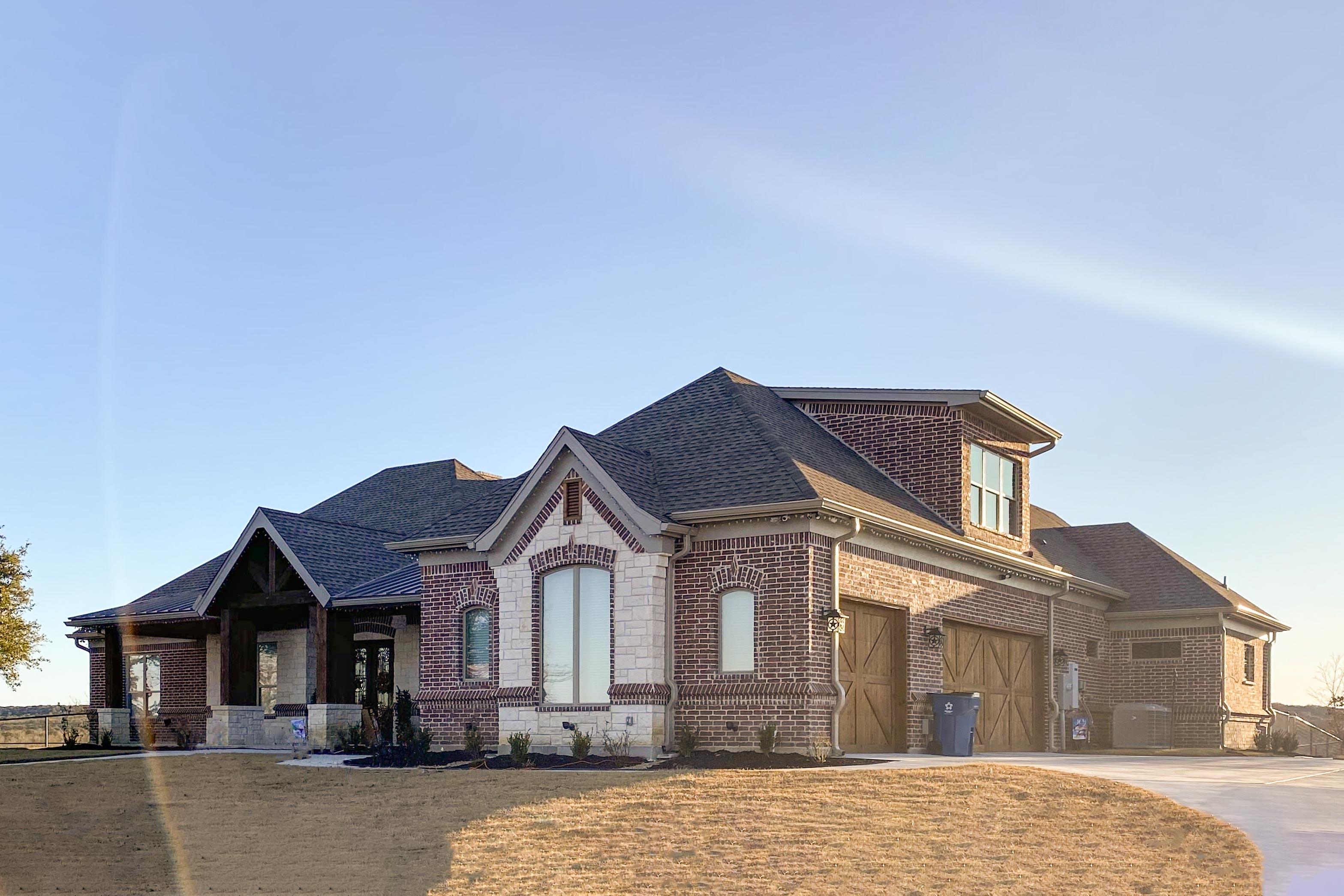 House plan exterior: Brick and stone facade, covered entry with timber posts, dormer, and attached three-car garage.
