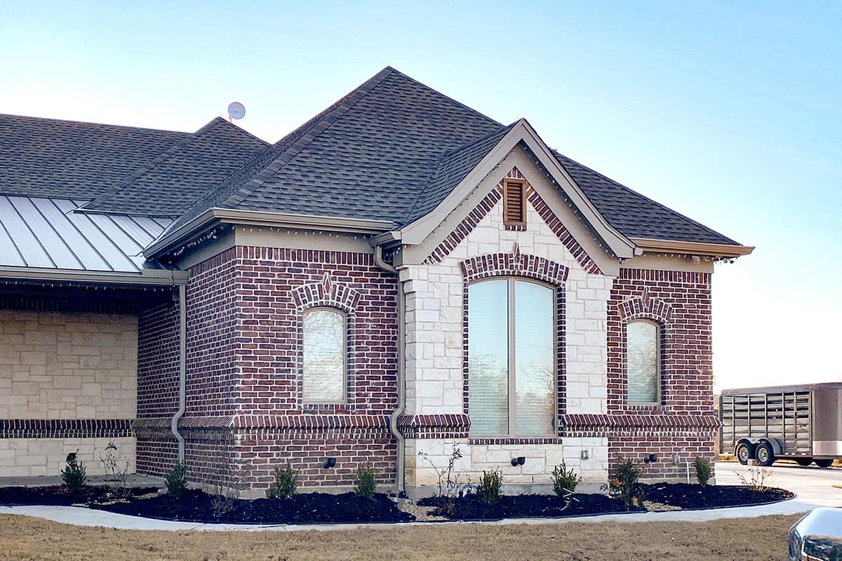 House plan exterior: Single-story home with brick and stone facade, pitched rooflines, and arched windows.