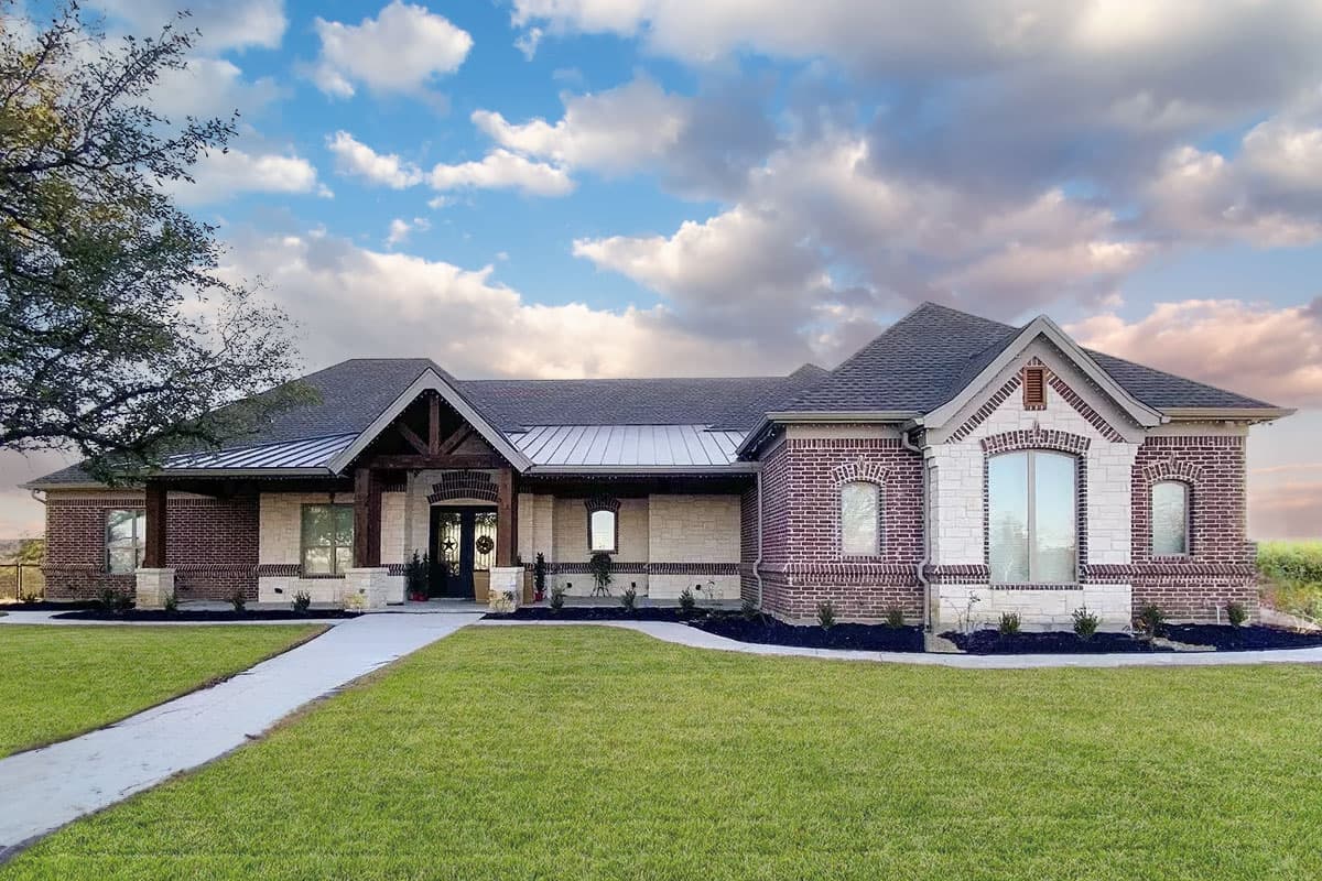 House plan exterior. One-story home with a gabled roof, brick and stone facade, and a covered porch with exposed beams.