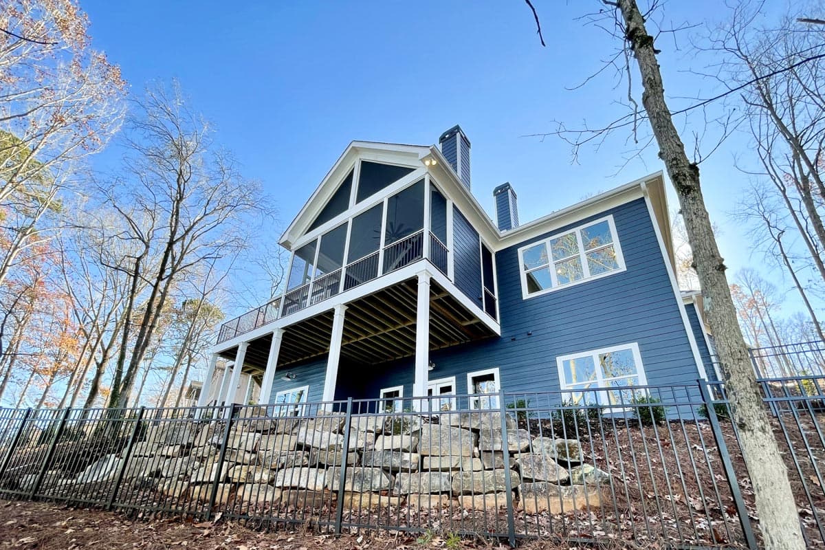 Modern house exterior with a large screened porch, deck, gabled roofline, and two chimneys.