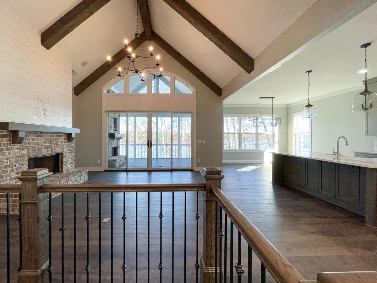 Great room with vaulted ceiling, exposed beams, brick fireplace, and large windows overlooking a scenic view.
