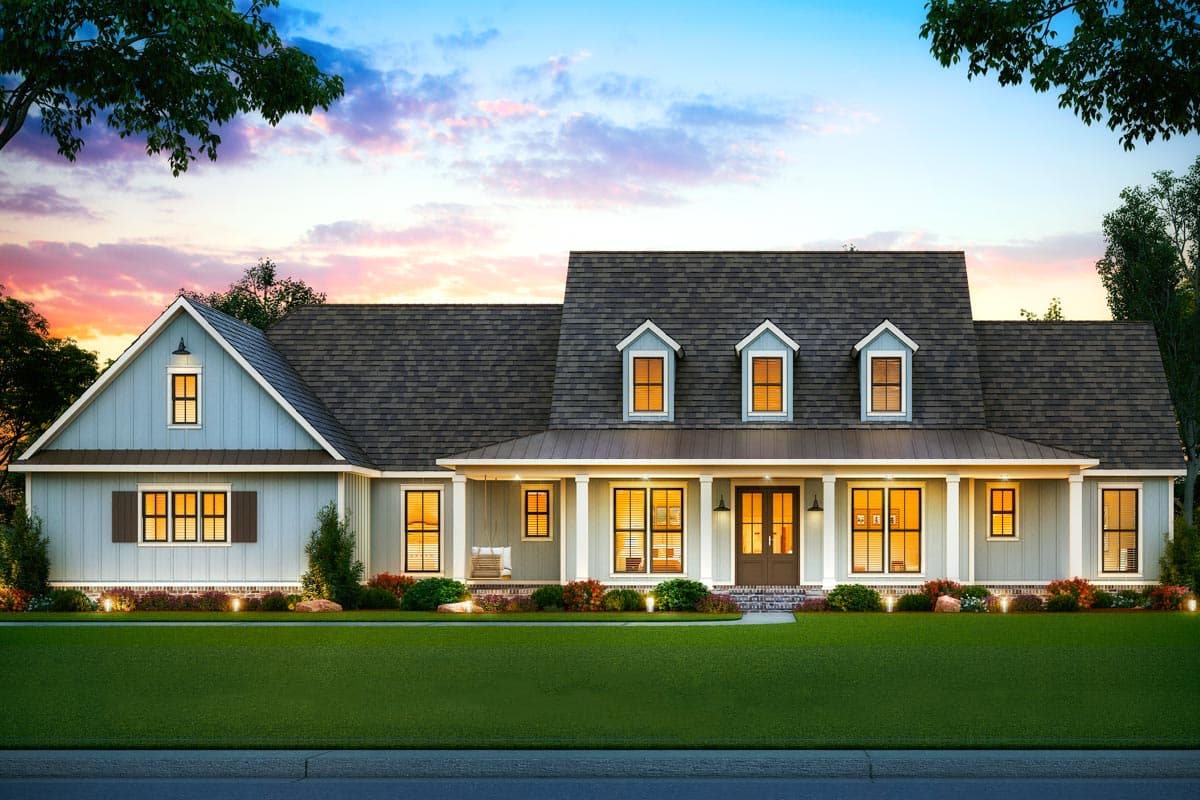 A large, light blue house with a dark gray roof at sunset. The home features a front porch, multiple windows, and a well-manicured lawn.