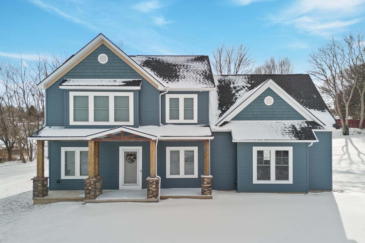 Two-story house plan exterior with gables, dormers, shingle siding, and a covered porch with stone-clad columns.