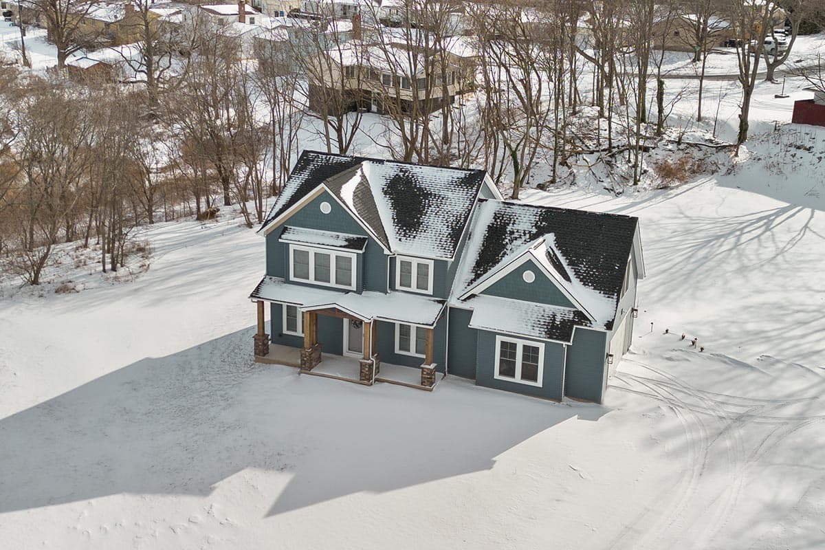 Two-story house plan exterior with prominent gables, a covered front porch with stone and wood posts, and an attached garage.