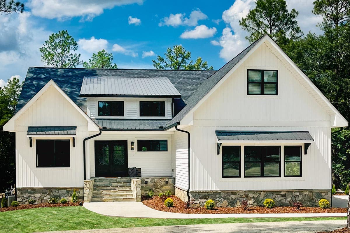 Modern Farmhouse house plan exterior with white board and batten siding, stone foundation, metal roof accents, and black awnings.