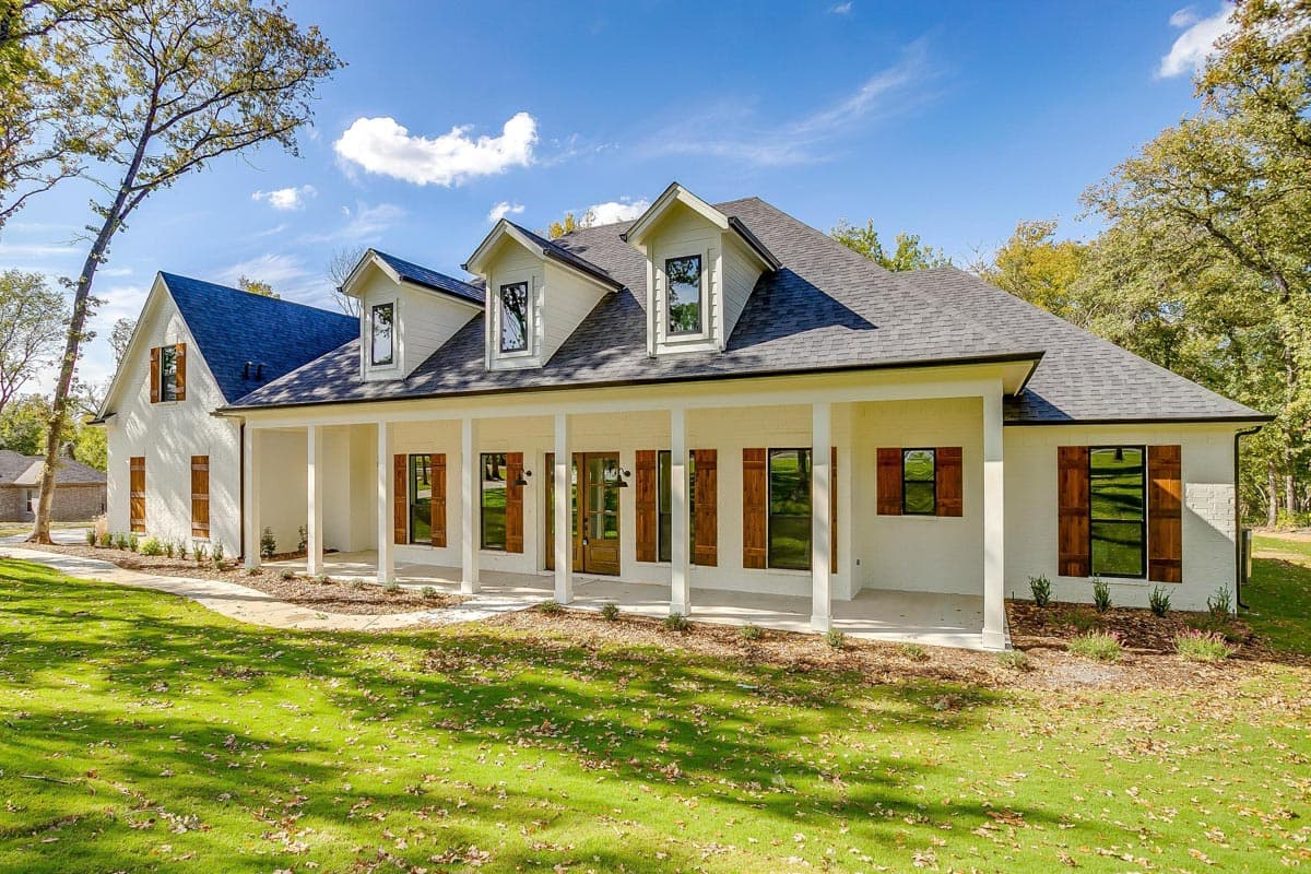 House plan exterior with Craftsman style. Features include a long covered porch, gables, dormers, and a dark shingle roof.
