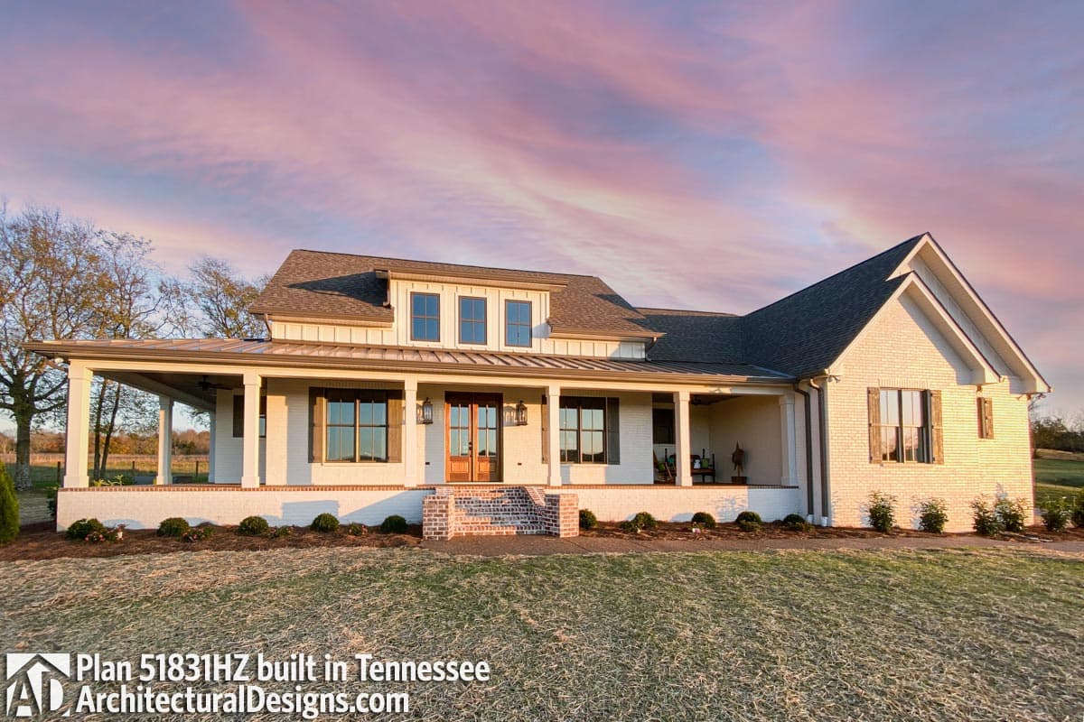 House plan exterior: Modern Farmhouse style, two stories, wide covered porch with columns, dormers, and brick accents.