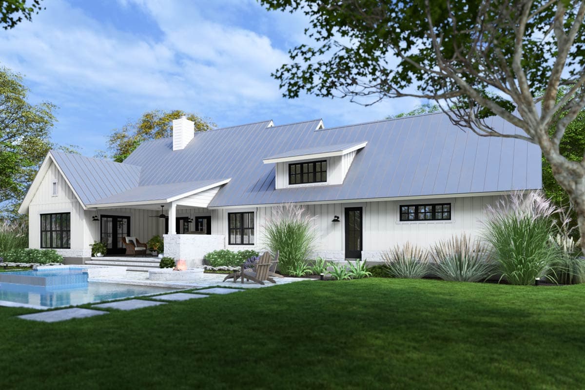 A modern white farmhouse with a metal roof, swimming pool, and a manicured lawn, the setting is a sunny day.