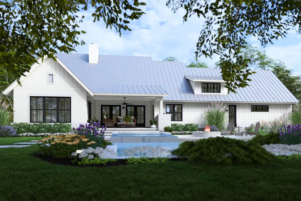 A modern white farmhouse with a pool and fire pit in the backyard. The house has a metal roof and black window frames and doors.