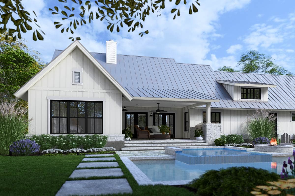 A modern white farmhouse with a metal roof, black-framed windows, and a patio overlooking a pool, surrounded by manicured landscaping.