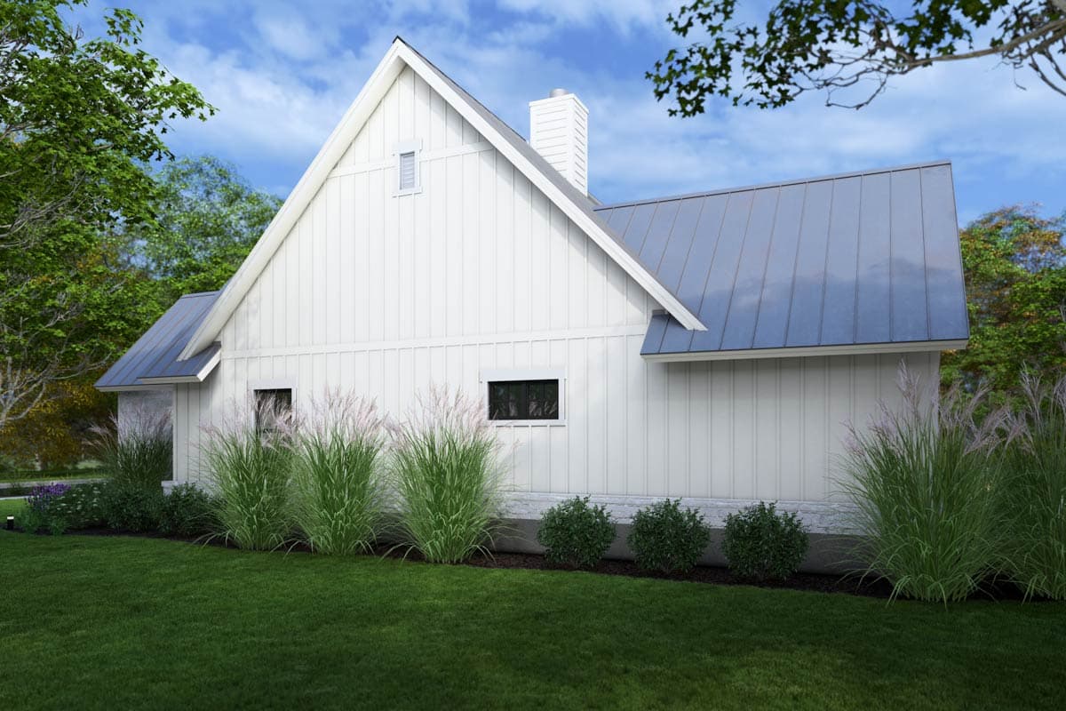 A modern white house with a blue metal roof sits among lush green grass and ornamental grasses. Blue sky and trees surround it.