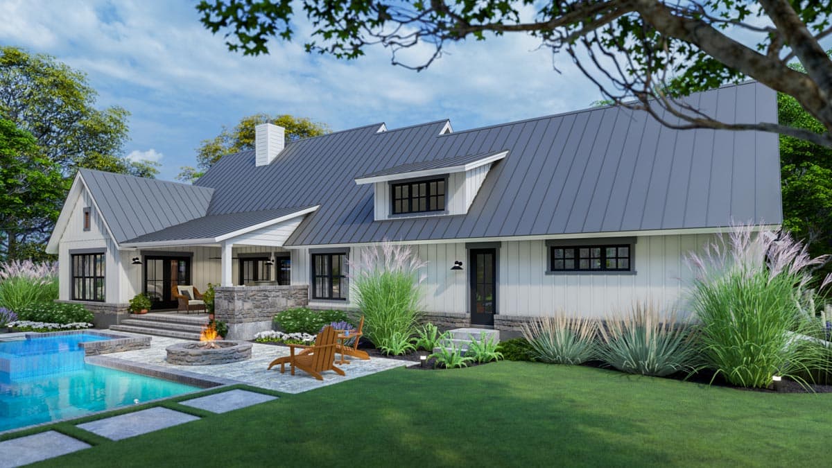 A modern farmhouse with a pool, fire pit, and comfortable seating. The home features a dark gray metal roof, white siding, and lush landscaping.