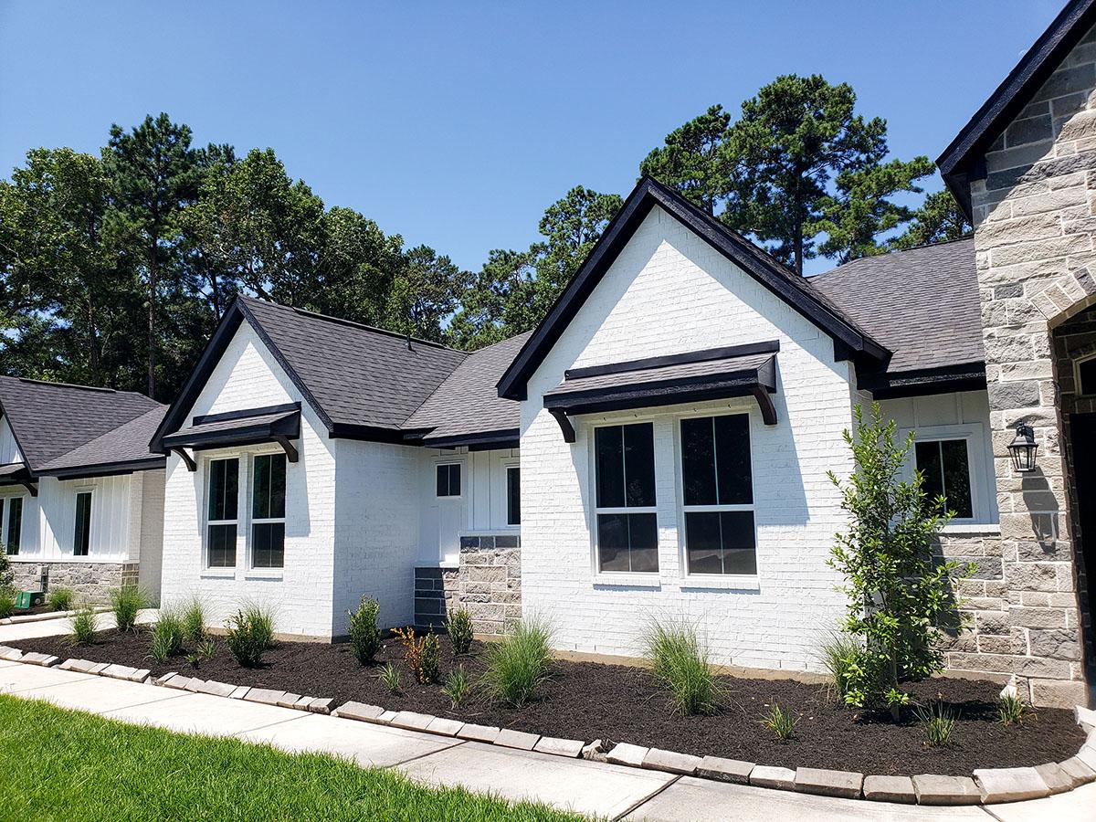 House plan exterior. White brick one-story home with stone accents, dark gables, and asphalt roof.