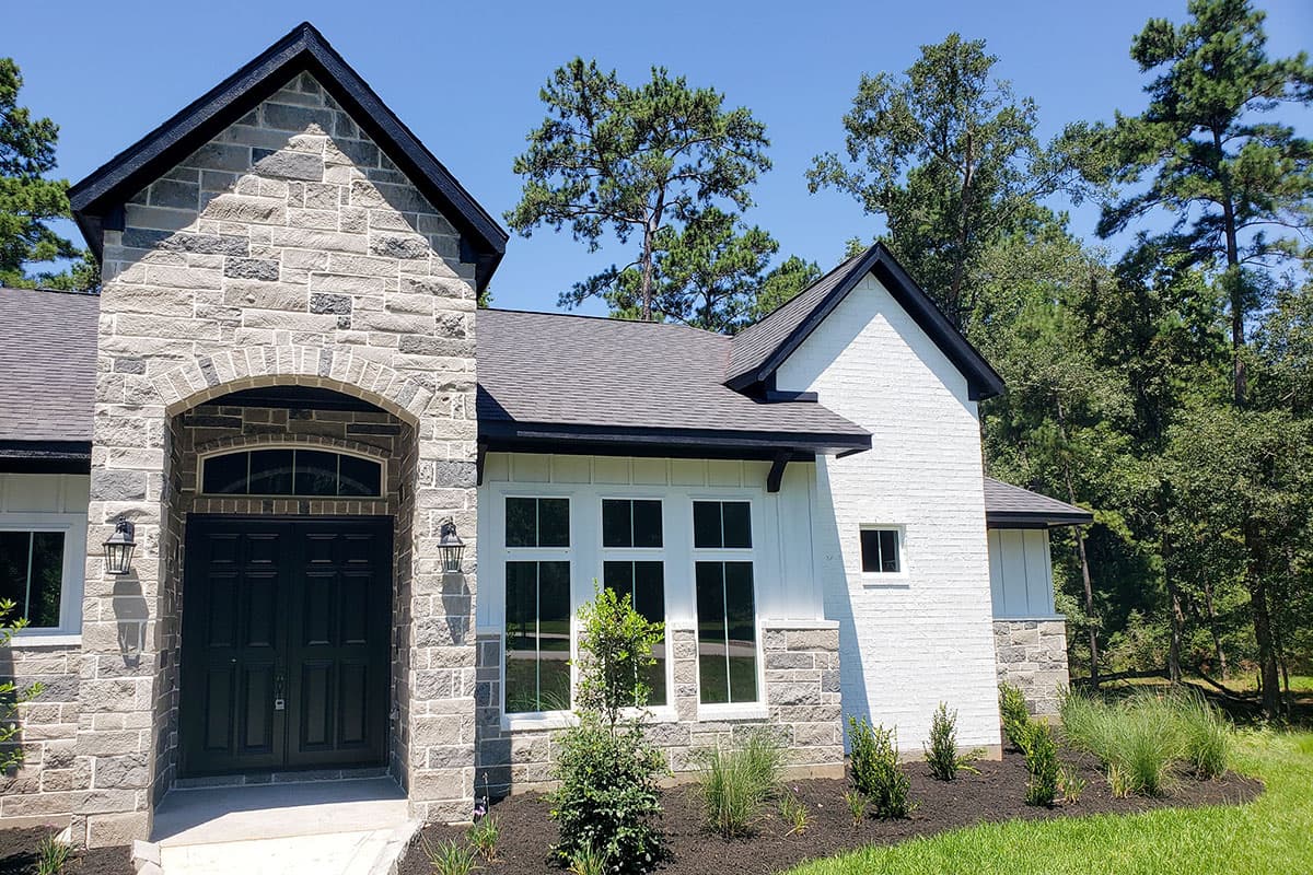 House plan exterior with stone facade, arched entryway with double doors, large multi-pane windows, and gabled roof.